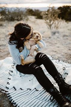 a woman sitting on top of a blanket holding a dog