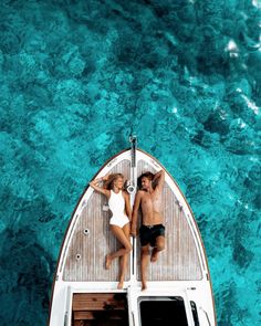 two people laying on the back of a boat in clear blue water, top view