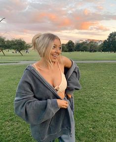 a woman is standing in the grass with her arms around her shoulders and smiling at the camera