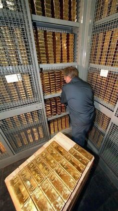 a man looking at some gold bars in a room filled with metal shelvings