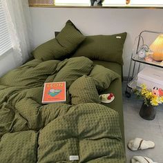 a bed with green comforter and pillows on it next to a lamp, flowers and other items