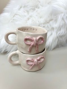 two mugs with pink bows on them sitting next to each other in front of a white furnishing