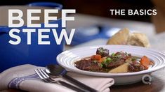 a white plate topped with beef stew next to a blue pot and silver utensils