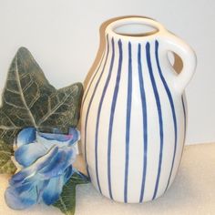 a blue and white striped vase next to a leaf