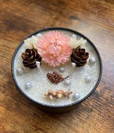 a bowl filled with water and flowers on top of a wooden table next to pine cones