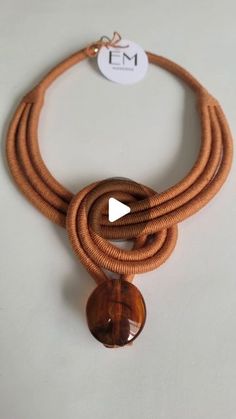 a brown necklace with a glass bead hanging from it's center, on a white surface