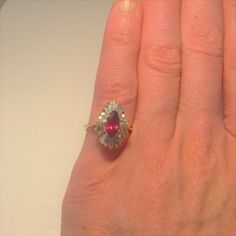 Here we have a gorgeous vivid red natural ruby and diamond ballerina style engagement ring dating to the mid century era. At the heart of this gorgeous ring sits a 1.30 carat marquise cut natural earth mined ruby. This large ruby measures approximately 9.50mm x 5.22mm x 3.60mm. Surrounding this exceptional gem quality ruby there is a halo of diamond accents set into a ballerina tiered setting. There are ten baguettes and eighteen round brilliant cut diamonds all VS clarity and G/H/I in color. Th Red Baguette Cut Diamond Accent Rings, Fine Jewelry Pear-shaped Ruby Ring With Diamond, Red Ruby Ring With Brilliant Pear-shaped Cut, Red Pear-shaped Ruby Ring With Brilliant Cut, Baguette Cut Ruby Ring For Anniversary, Pear-shaped Ruby Ring With Rose Cut Diamonds For Wedding, Pear-shaped Ruby Rings With Rose Cut Diamonds, Fine Jewelry Ruby Ring With Marquise Halo, Fine Jewelry Marquise Ruby Ring With Halo Setting