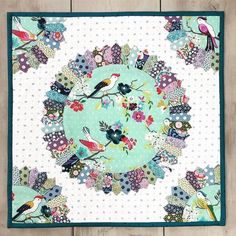 a quilted table runner with birds and flowers in the center on a wooden surface