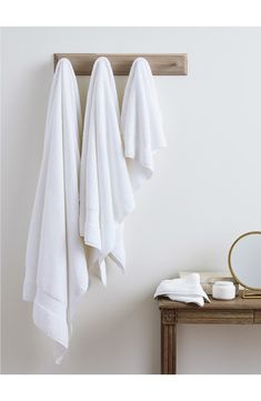 three white towels hanging on the wall next to a table with a mirror and soap dispenser