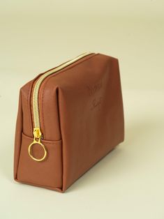 a brown leather pouch with a gold ring on the front and side zipper open to show it's contents