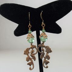 "An adorable new pair of crystal earrings with Swarovski crystals in a pretty pale emerald green, with a brass component with a gingko and ivy leaf pattern. These have a Victorian feel and are very lightweight! These one of a kind earrings measure 2 1/4\" and will arrive beautifully packaged. To see more jewelry and handmade beads, click here: https://www.etsy.com/shop/StoneDesignsbySheila?ref=hdr_shop_menu" Handmade Green Crystal Metal Earrings, Green Crystal Earrings For Jewelry Making, Pierced Green Copper Earrings, Green Copper Pierced Earrings, Elegant Green Copper Earrings, Green Dangle Jewelry With Bead Caps, Lampwork Bead Earrings, Green Antique, Classy Earrings