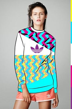 a woman in shorts and a sweater with an adidas logo on the front, standing against a multi - colored background