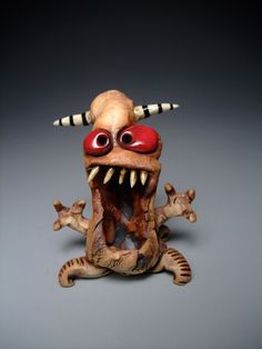 a ceramic sculpture of a demon with horns and fangs on it's head, sitting in front of a gray background