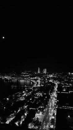 an aerial view of a city at night with lights on the street and bridge in the distance