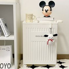 a mickey mouse keychain on top of a white radiator next to a book shelf