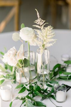 white flowers and greenery in glass vases on a table