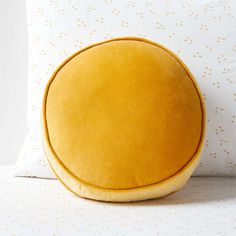 a yellow round pillow sitting on top of a white bed next to a pillow case