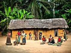 a group of people standing in front of a hut with grass roof and palm trees