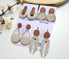 three pairs of earrings on top of a table next to white flowers and a piece of paper