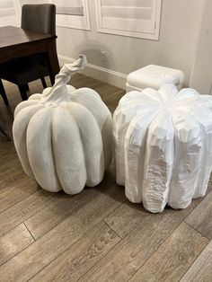 two large white pumpkins sitting on top of a wooden floor next to each other