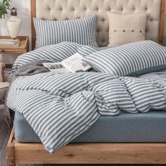 a bed with blue and white striped comforter on it, next to a wooden headboard