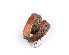 two brown leather bracelets sitting on top of each other, one with an intricate design