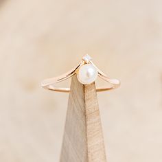 a ring with a pearl sits on top of a wooden stand