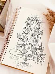 a drawing of a woman with flowers on her head sitting next to an open notebook