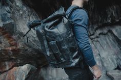 a man wearing a black leather backpack standing in front of some rocks