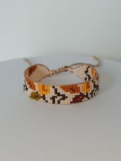 a close up of a beaded bracelet on a white surface with an orange, yellow and brown design