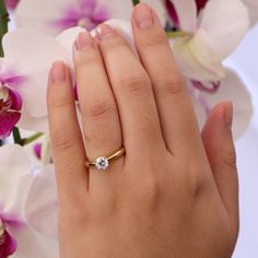 a woman's hand with a diamond ring on it and flowers in the background