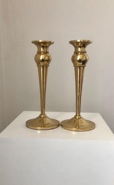 two golden candlesticks sitting on top of a white table next to each other