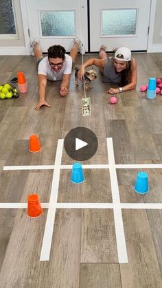 two people are laying on the floor playing with plastic cups and an interactive board game