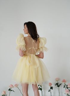 Introducing the Britney Dress in a delightful light yellow: a stunning creation crafted from delicate bubble organza. This lightweight dress features an elegant silhouette with a voluminous floating skirt that moves gracefully with every step. The charming puff sleeves add a whimsical touch, making it perfect for any special occasion. The Britney Dress is enclosed with delicate bow ties down the back, adding a romantic and feminine detail that completes the look. In light yellow, this dress exud Light Yellow Dress Wedding, Dress Modeling Poses, Spring Fairy Dress With Puff Sleeves And Ruffles, Beige Balletcore Dress For Party, Organza Puff Sleeve Wedding Dress, Wedding Puff Sleeve Dress With Ruffles And Balloon Sleeves, Balletcore Puff Sleeve Party Dress, Spring Princess Style Puff Sleeve Dress With Ruffles, Spring Princess Puff Sleeve Dress With Ruffles