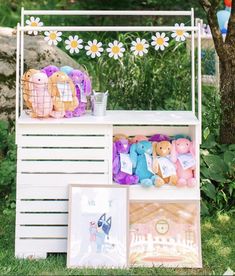 a white shelf with stuffed animals on it in the grass next to a tree and flowers