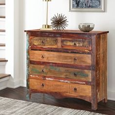 an old dresser with wooden drawers in a living room next to stairs and a painting on the wall