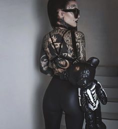 a woman with tattoos is holding a cat and wearing black leggings while standing against a wall