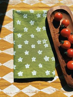 tomatoes in a wooden tray on a yellow and white checkered tablecloth next to a green napkin