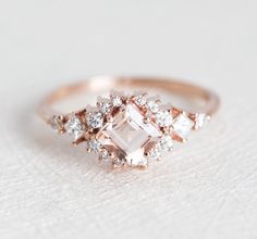 an engagement ring with diamonds on the sides and a pink diamond in the middle, sitting on top of a white surface