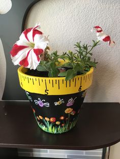 a potted plant with flowers and a measuring tape around it on a table next to a wall