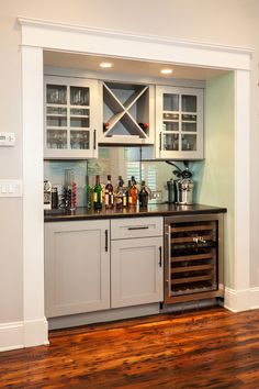 a kitchen with white cabinets and wood flooring next to a wine rack filled with bottles