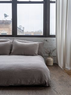 a bed sitting in front of a window next to a wooden floor and white curtains