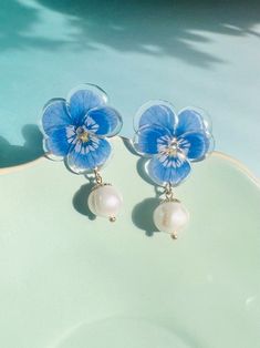 These handmade earrings feature delicate blue pansy flowers crafted from shrink plastic, adorned with freshwater pearl drops that add a touch of elegance. Perfect as a gift for her or as "something blue" for a special occasion, these dangling earrings combine charm and sophistication in one exquisite piece of jewelry. Whimsical Blue Flower Earrings, Blue Pansy Flower, Blue Flower-shaped Party Earrings, Blue Flower-shaped Spring Jewelry, Delicate Blue Flower-shaped Earrings, Blue Pansy, Blue Flower Earrings, Pansy Flowers, Shrink Plastic Jewelry