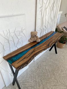 a small teddy bear sitting on top of a wooden bench next to a white wall