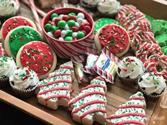 a wooden tray topped with lots of cupcakes and cookies next to christmas treats