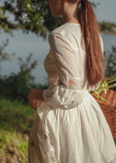 A dreamy ivory dress with floral embroidery on the net inserts, in tiers and shoulders. The tiny details in this dress are a delight. This dress is full length, buttons in front, also has a smocking detail on the waist. The romance of this dress comes to life with pink and sage flowers embroidered on the up-cycled net, the light weight cotton will make you feel like you're walking on clouds. IMPACT & CARE Made from upcycled materials Ethically made in Jaipur Hand wash in cold water FIT Your perf Delicate White Dress For Daywear, Spring Cottagecore Dress With Smocked Cuffs, White Feminine Prairie Dress For Garden Party, Feminine White Prairie Dress For Garden Party, Spring White Maxi Dress For Gatherings, White Spring Maxi Dress For Gatherings, Cottagecore Cream Dress With Floral Embroidery, White Maxi Dress For Spring Gatherings, Elegant Dress With Smocked Cuffs For Garden Party