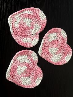 three crocheted coasters with pink and white designs on black table top next to each other