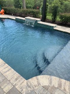 an empty swimming pool surrounded by stone pavers and brick walkways, with a water feature in the middle