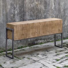 a wooden bench sitting on top of a stone floor next to a cement wall with metal legs