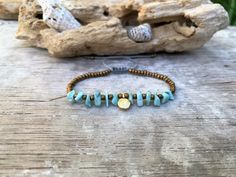 a beaded bracelet with blue beads and a gold disc on it sitting on top of a wooden table